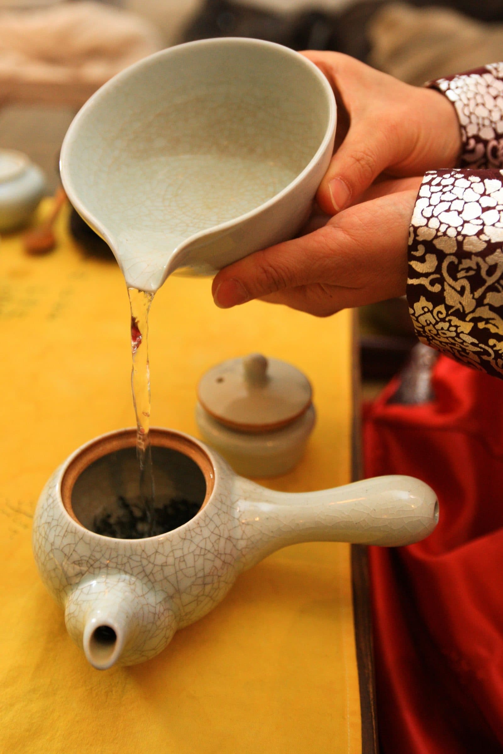 Hands pouring tea from a crackle-glazed ceramic bowl into a matching pot