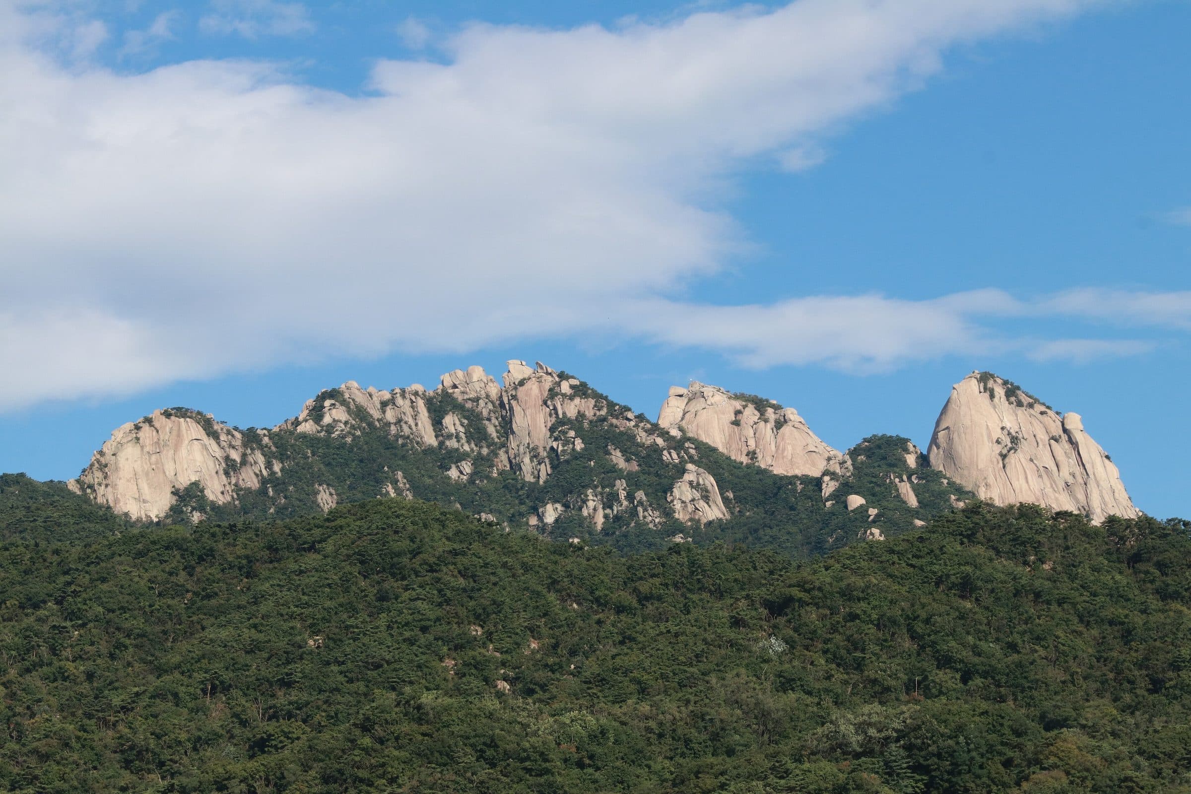 Granite peaks of Bukhansan rising above wooded slopes under a summer sky in Gyeonggi-do