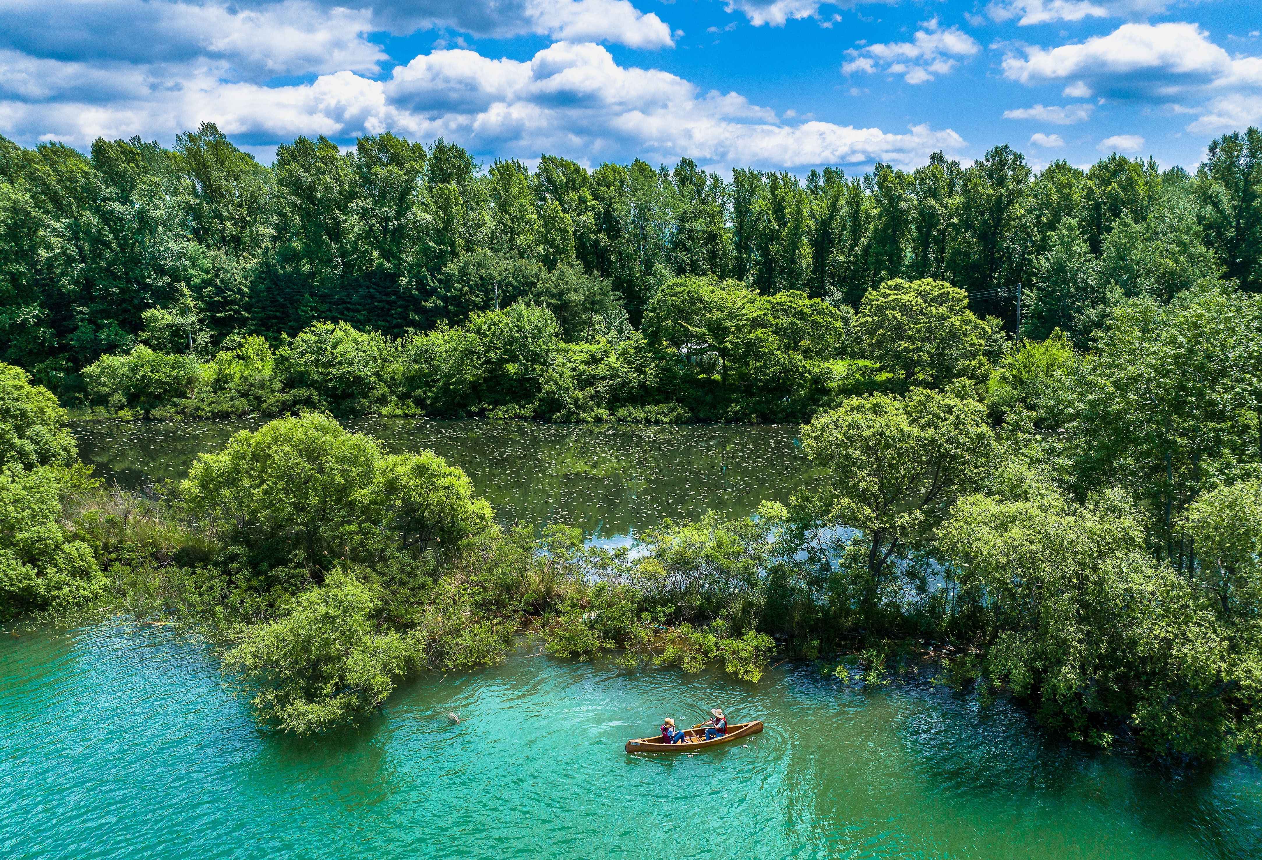 A small boat on turquoise water among wooded islets at Uiamho Lake in Chuncheon.